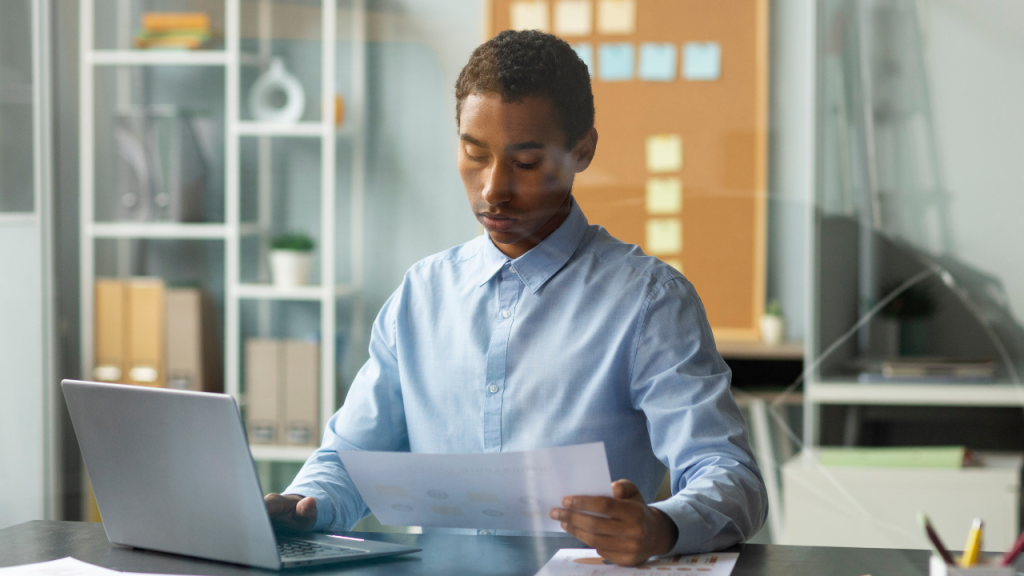 SME cash flow management: professional reviews paperwork beside a laptop in an office.